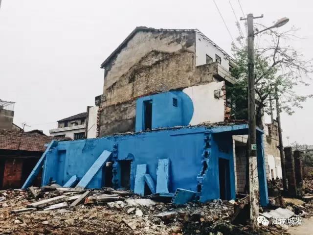△ 這棟建筑是臨江最近的半拆遷建筑物的遺留，沅江和堤壩成為了展覽的天然背景。創(chuàng)作團(tuán)隊(duì)對(duì)這棟建筑進(jìn)行了半涂裝，將符號(hào)性的沅水曲線(xiàn)與拆遷進(jìn)行中的建筑立面進(jìn)行意義的疊造，它們共同觸發(fā)了場(chǎng)所空間多元語(yǔ)境的生成，把拆遷這種暫時(shí)破壞性、干擾性的介入行動(dòng)與沅水右岸發(fā)展的未來(lái)性、美好性緊密融合。